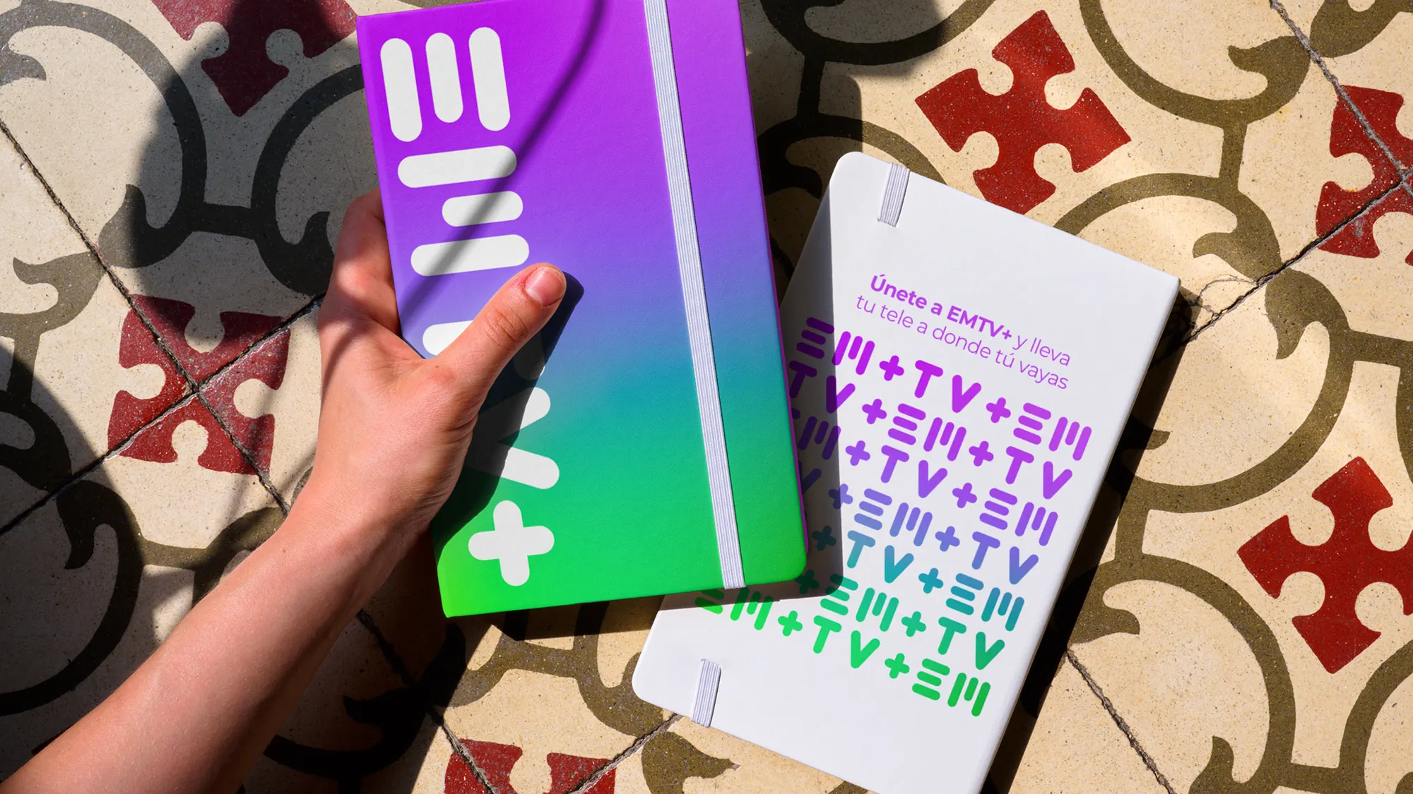 EMTV+ notebook and folder with the wordmark on a gradient cover and a repeated pattern insert